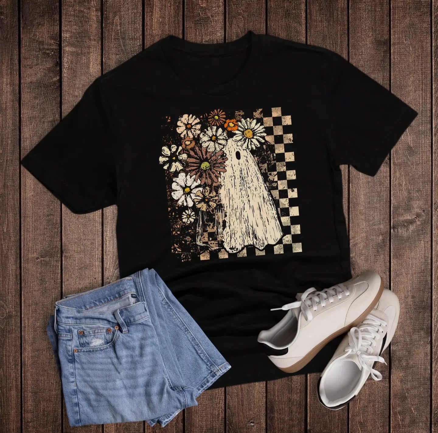 Black t-shirt with a graphic design on a wooden surface, accompanied by denim shorts and white sneakers.