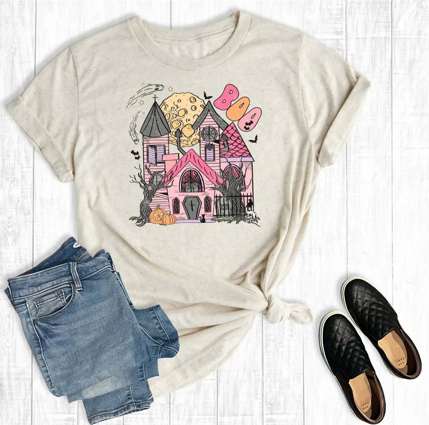 Beige t-shirt with a colorful graphic of a house, jeans, and black shoes on a white background