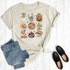 Beige t-shirt with graphic designs, blue jeans, and black shoes on a white wooden surface