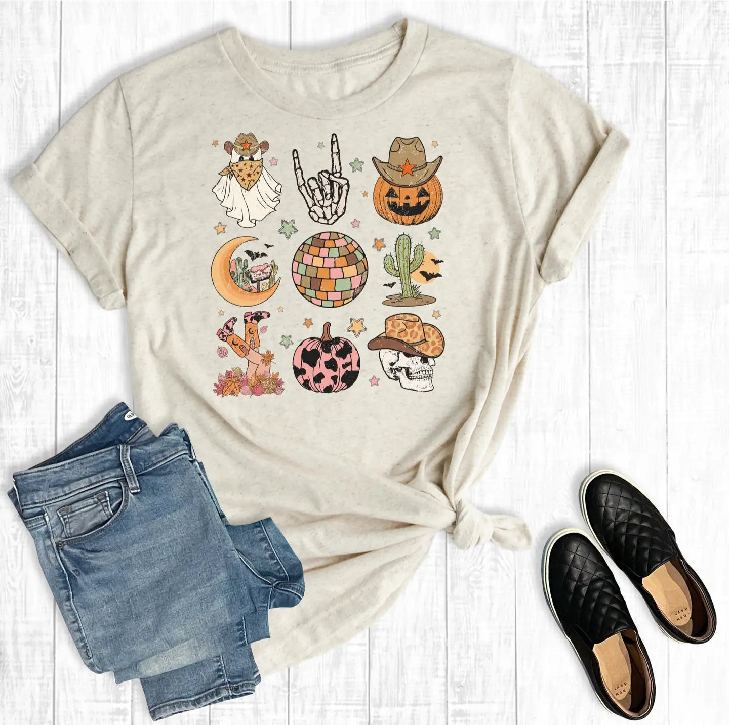 Beige t-shirt with graphic designs, blue jeans, and black shoes on a white wooden surface